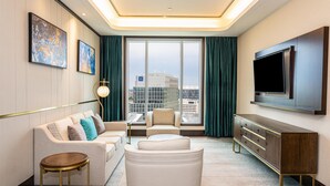 Habitació d'hotel moderna amb sofà, butaca, televisió i una finestra gran amb cortines.