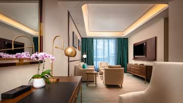 A modern hotel room with a large mirror, a desk with a laptop, a sofa, a chair, a TV, and a cabinet.
