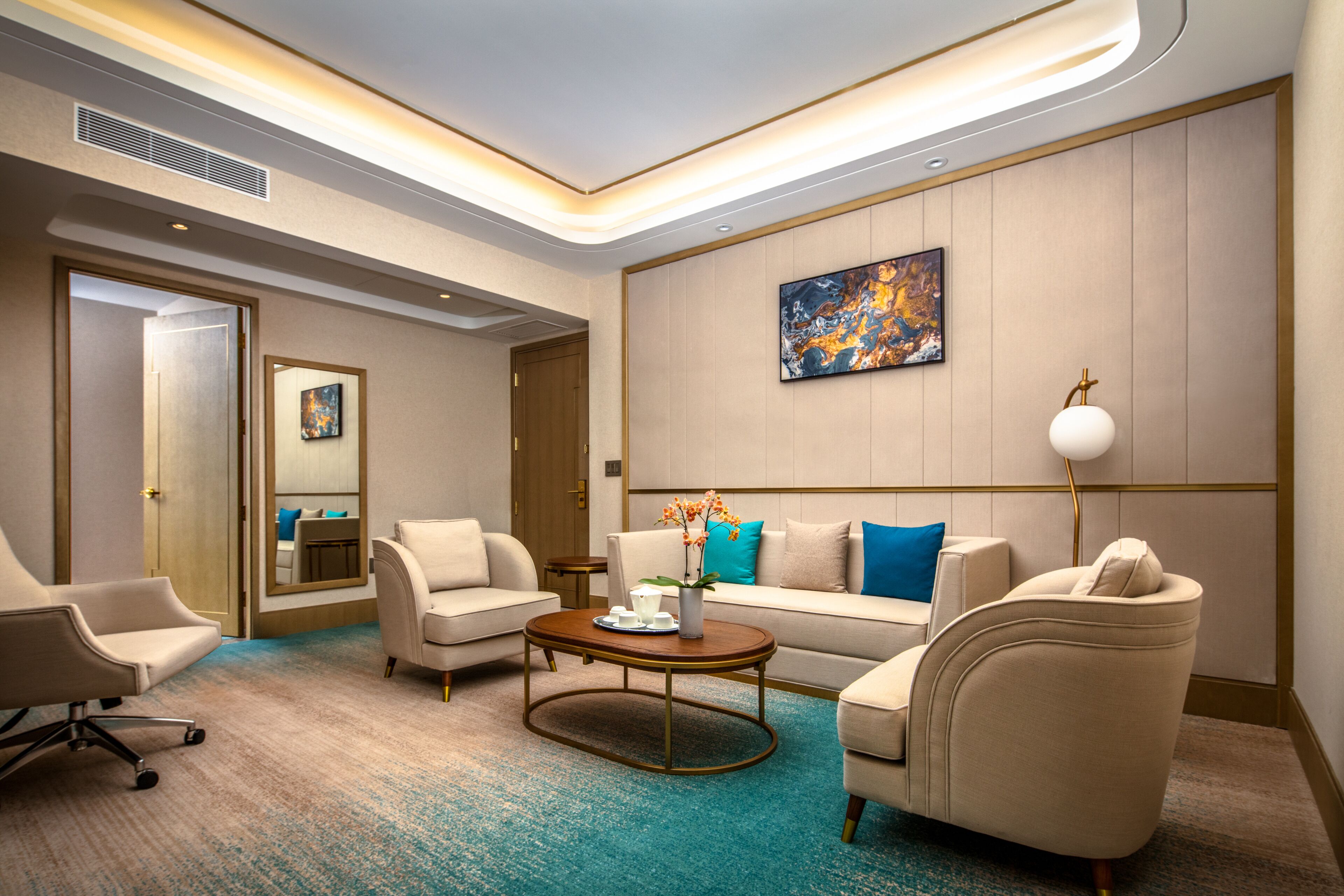 A modern hotel room with a sofa, armchairs, a coffee table, and a painting on the wall.