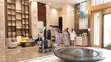 A spacious lobby with a marble floor, a reception desk, a large fountain, and a wall of shelves with various items.