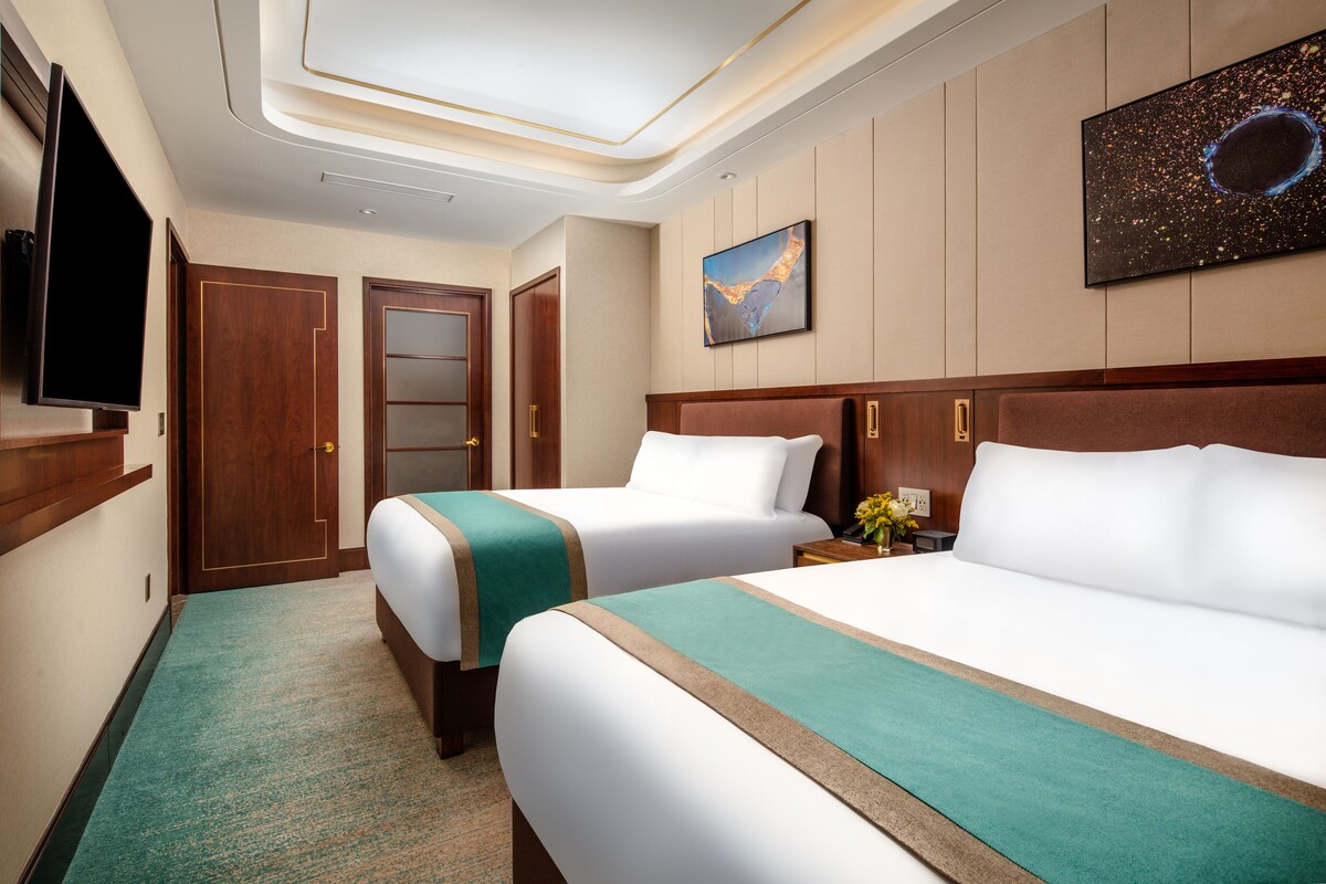 A hotel room with two beds, a television, a painting, and a carpeted floor.