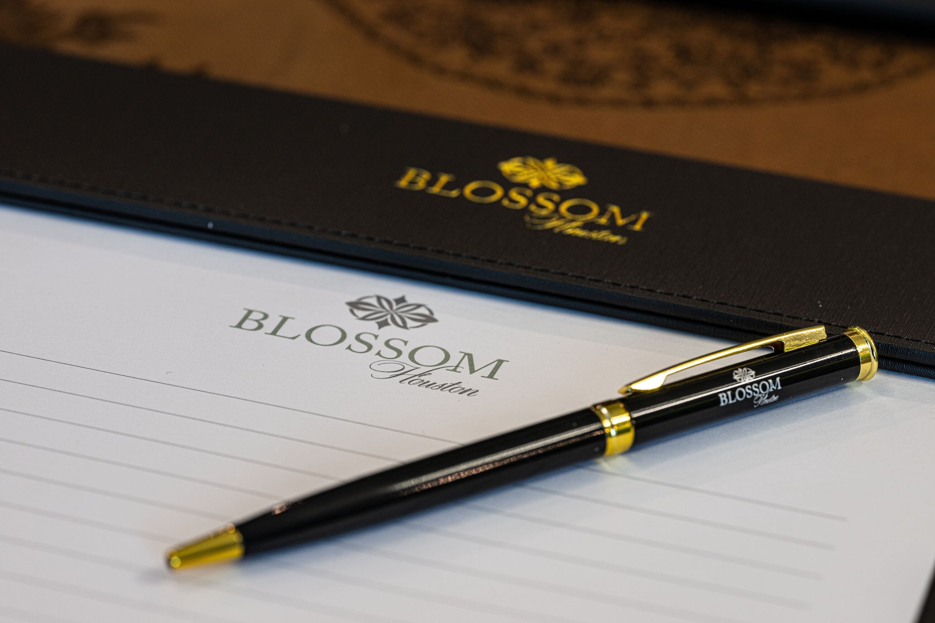 Uma caderneta preta com a inscrição em relevo 'BLOSSOM Houston' na capa e uma caneta sobre ela.