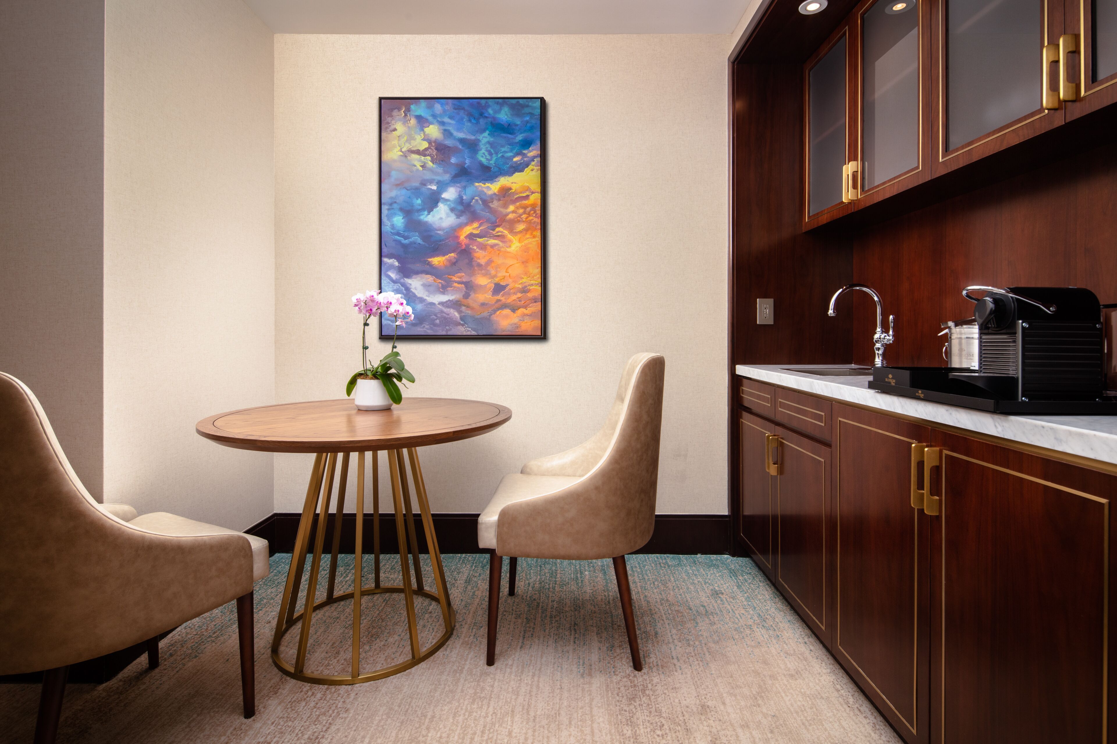 Une cuisine moderne avec des meubles en bois, une table de salle à manger ronde accompagnée de deux chaises, et un tableau abstrait aux couleurs vives accroché au mur.
