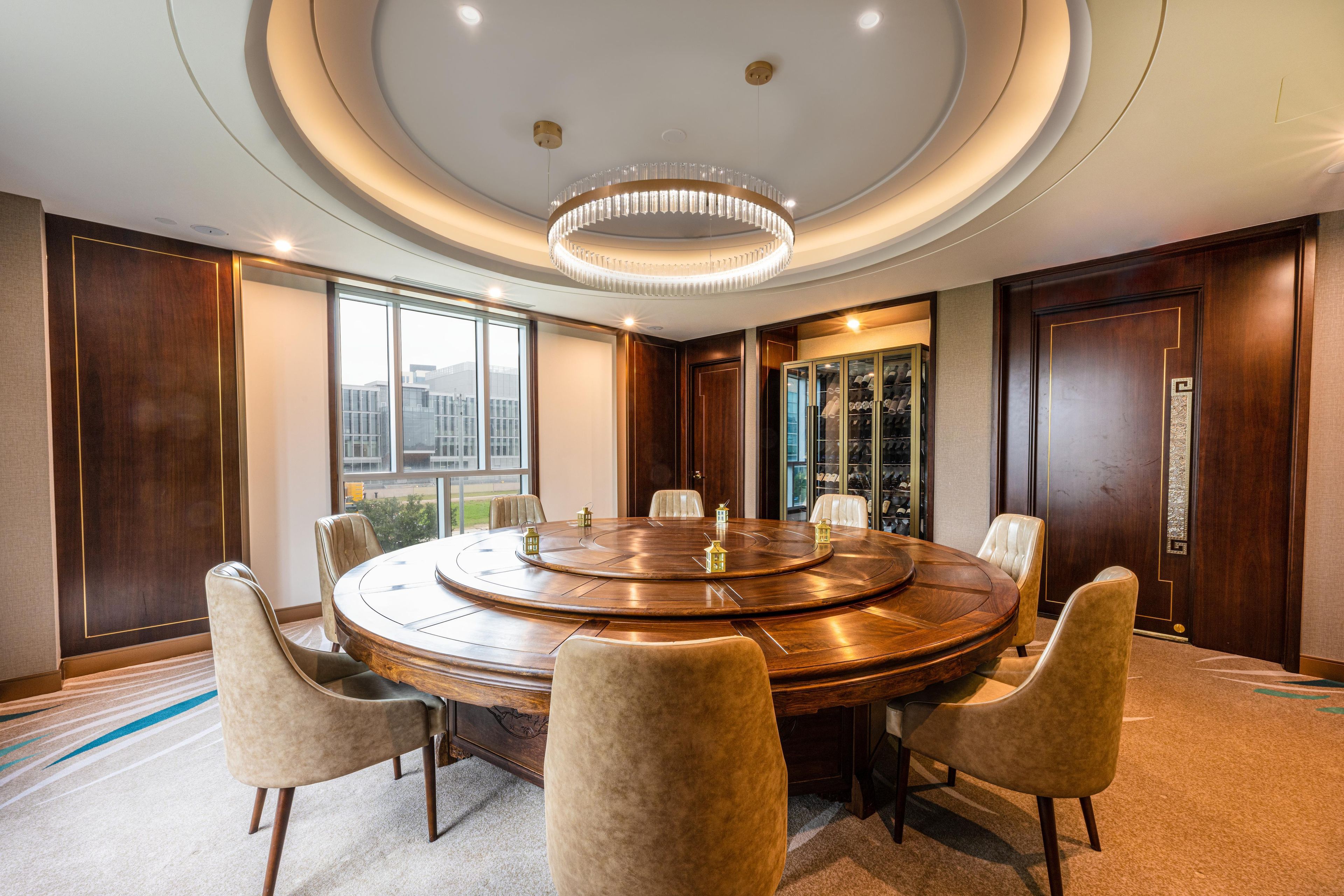 A conference room with a round table, chairs, a chandelier, and large windows.