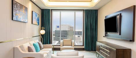 A modern hotel room with a sofa, armchair, and a TV mounted on the wall.