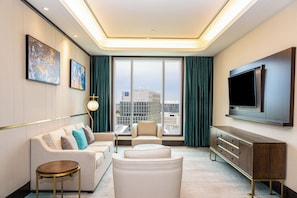 A modern hotel room with a sofa, armchair, and a TV mounted on the wall. - Blossom Hotel Houston, Curio Collection by Hilton (Houston)