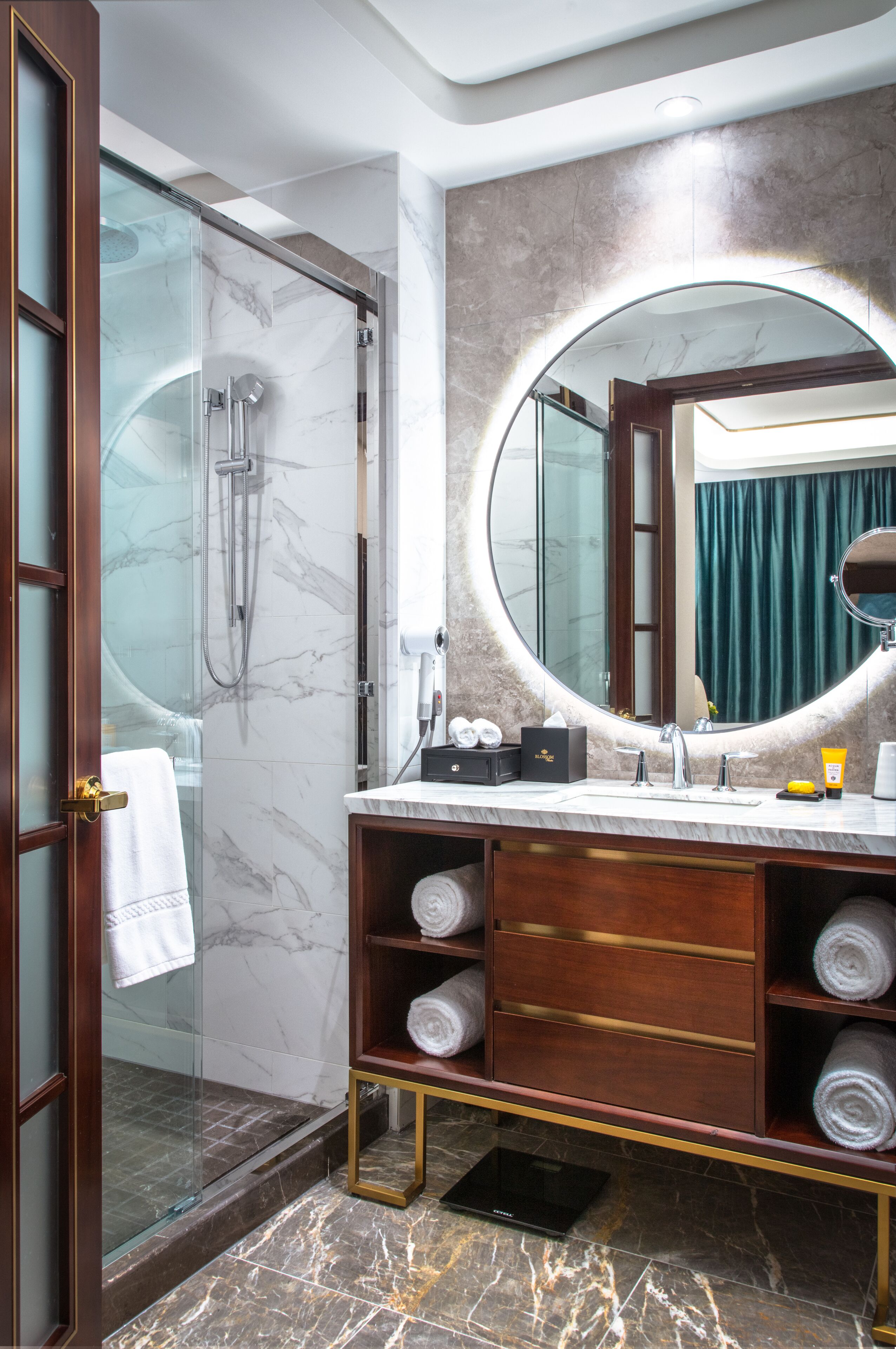 Ein modernes Badezimmer mit einer Glaskabine zur Dusche, einem Marmorboden, einem Holzanbau mit Handtüchern und einem großen Spiegel.