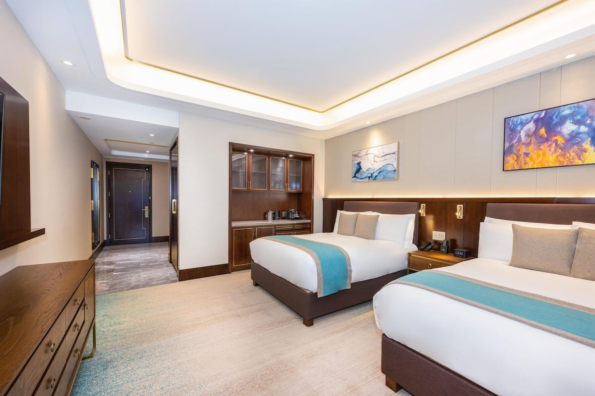 A hotel room with two beds, a desk, a wardrobe, and a painting on the wall.