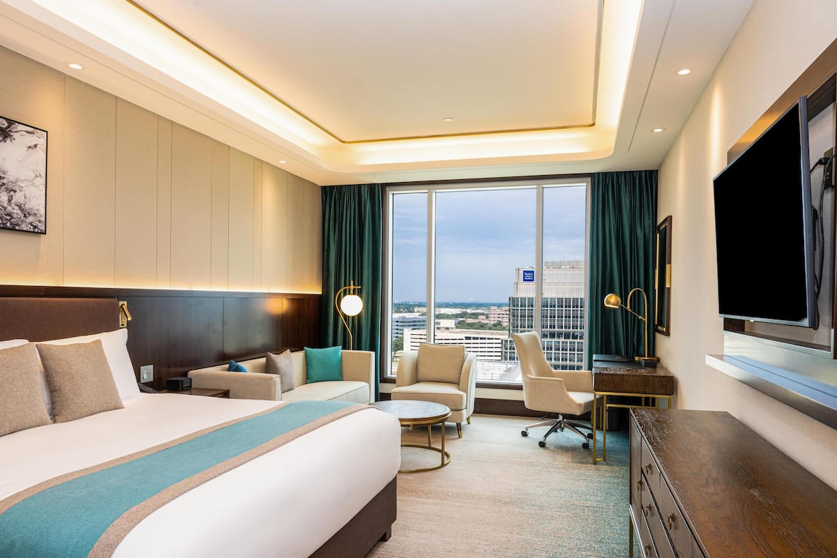 A modern hotel room with a large bed, a desk, a chair, and a TV.