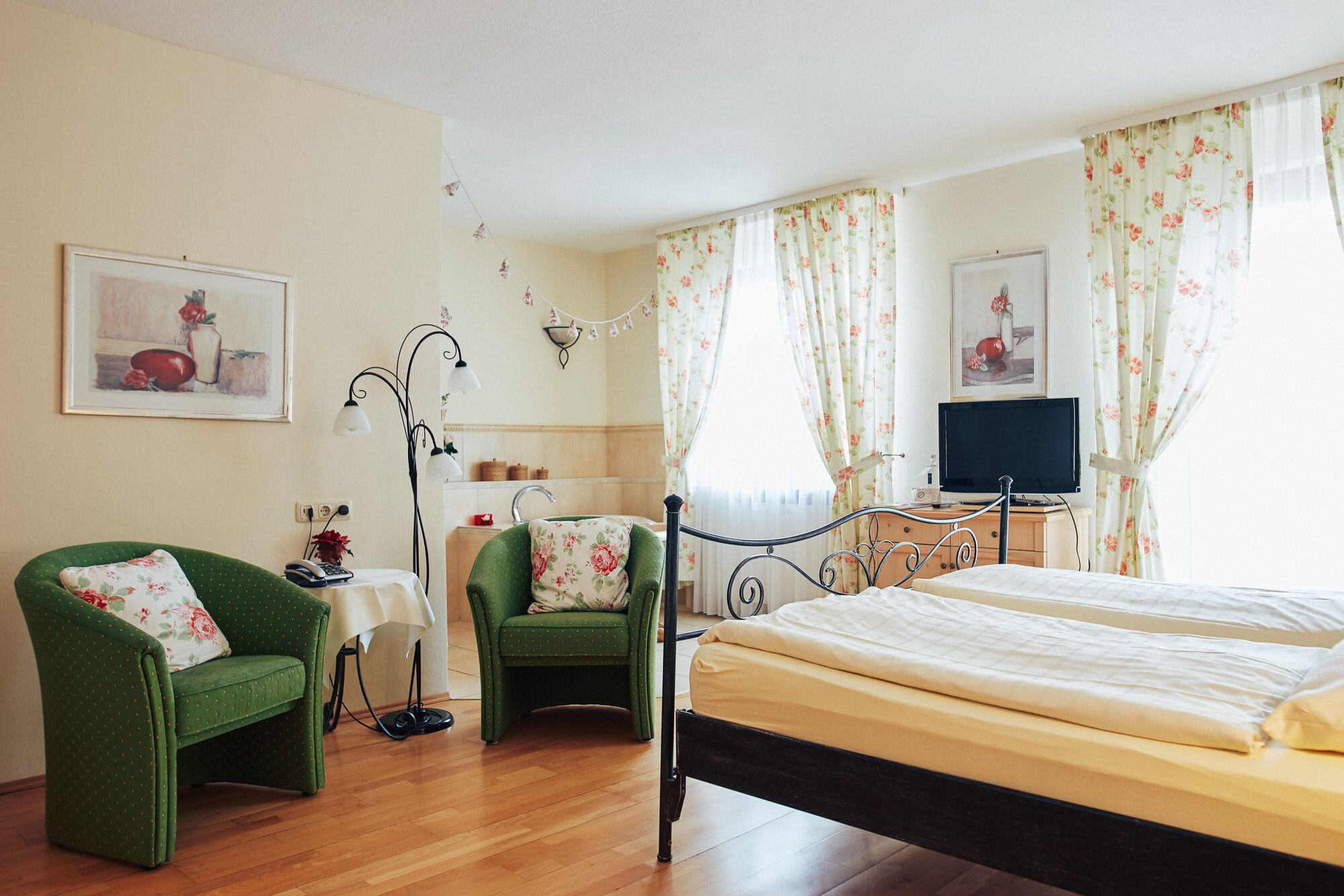 Une chambre à coucher avec un lit, deux chaises, un bureau, une télévision et des rideaux à motifs floraux.