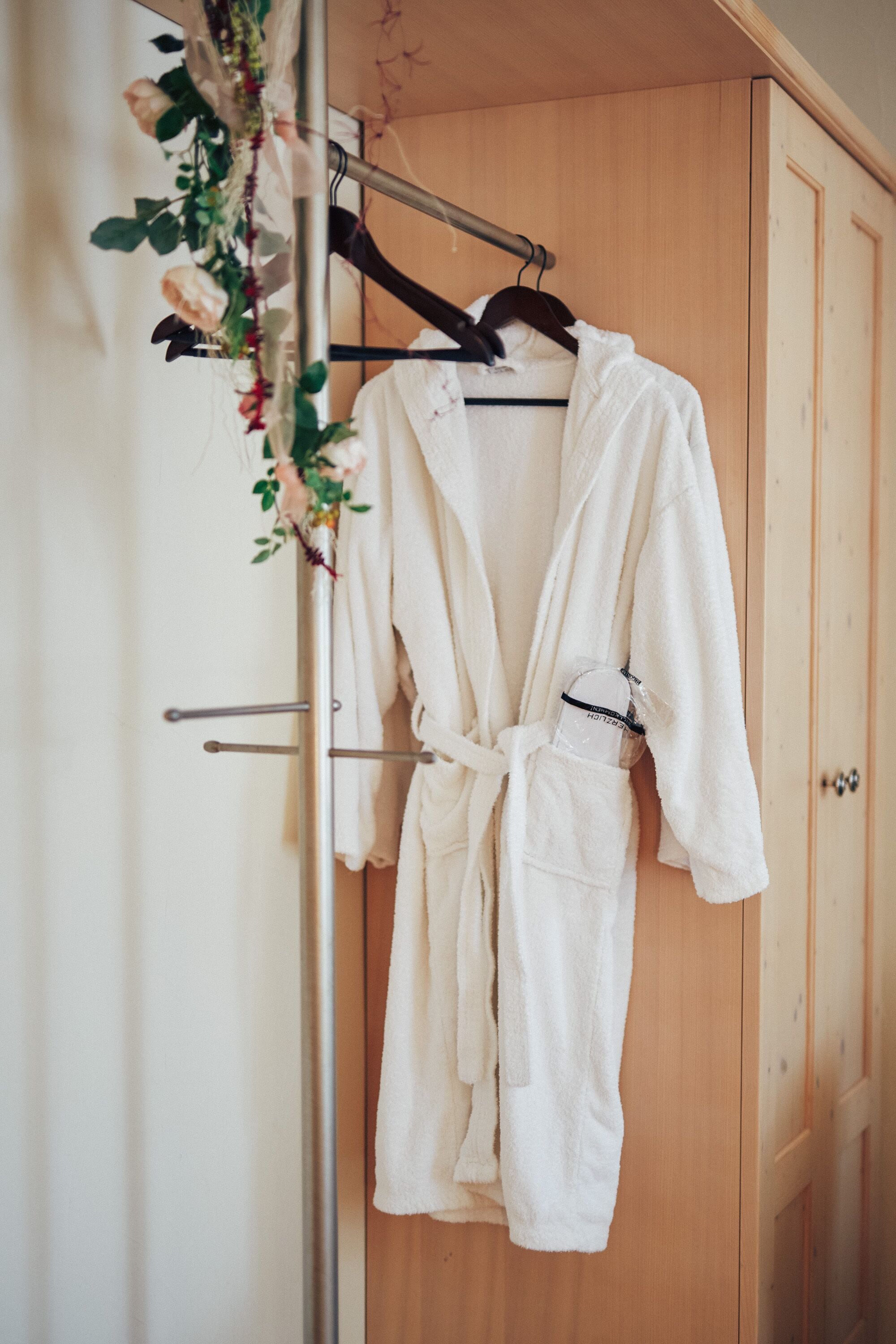 A wooden wardrobe with a white robe hanging on a metal rack.