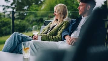 Two people sitting on a bench outdoors with a glass of wine in front of them.