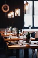Un restaurant dont les tables sont dressées pour le service, avec des luminaires suspendus et des plantes en pot.