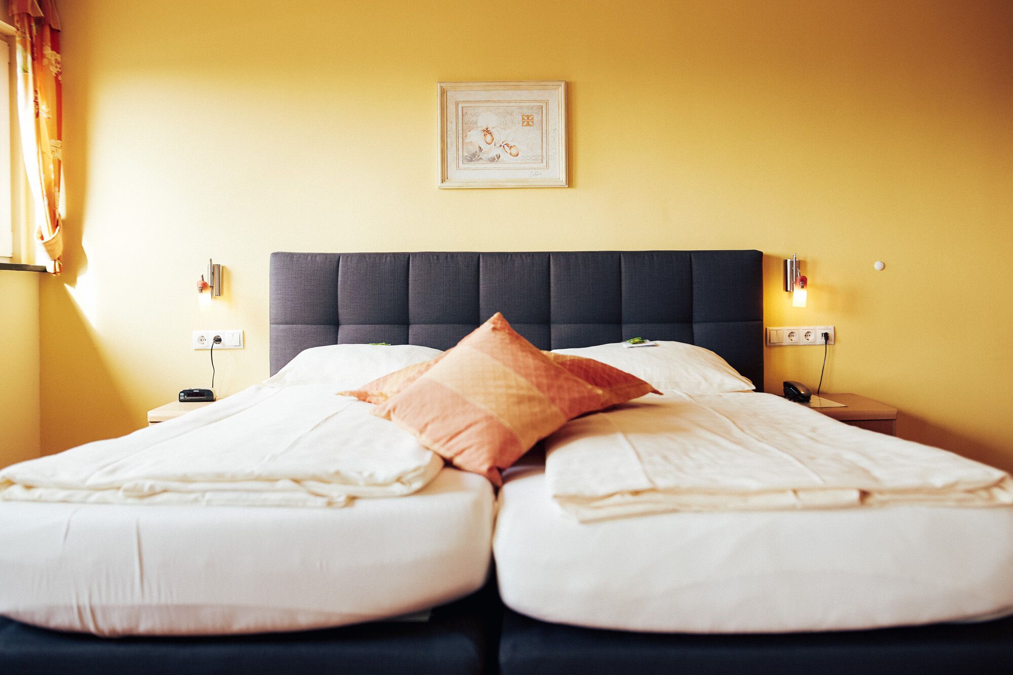 Un lit double avec une tête de lit sombre, deux tables de chevet avec des lampes et un tableau encadré au mur.