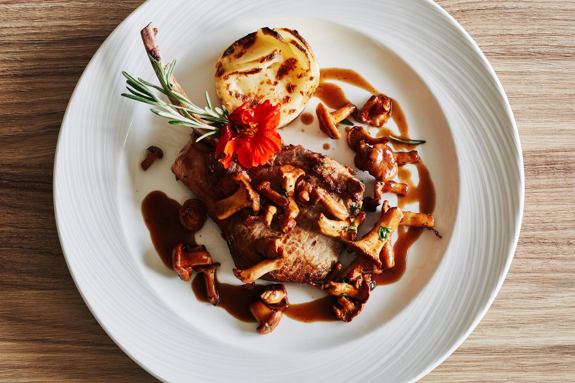 A white plate with a grilled meat dish, mushrooms, and a roasted potato.