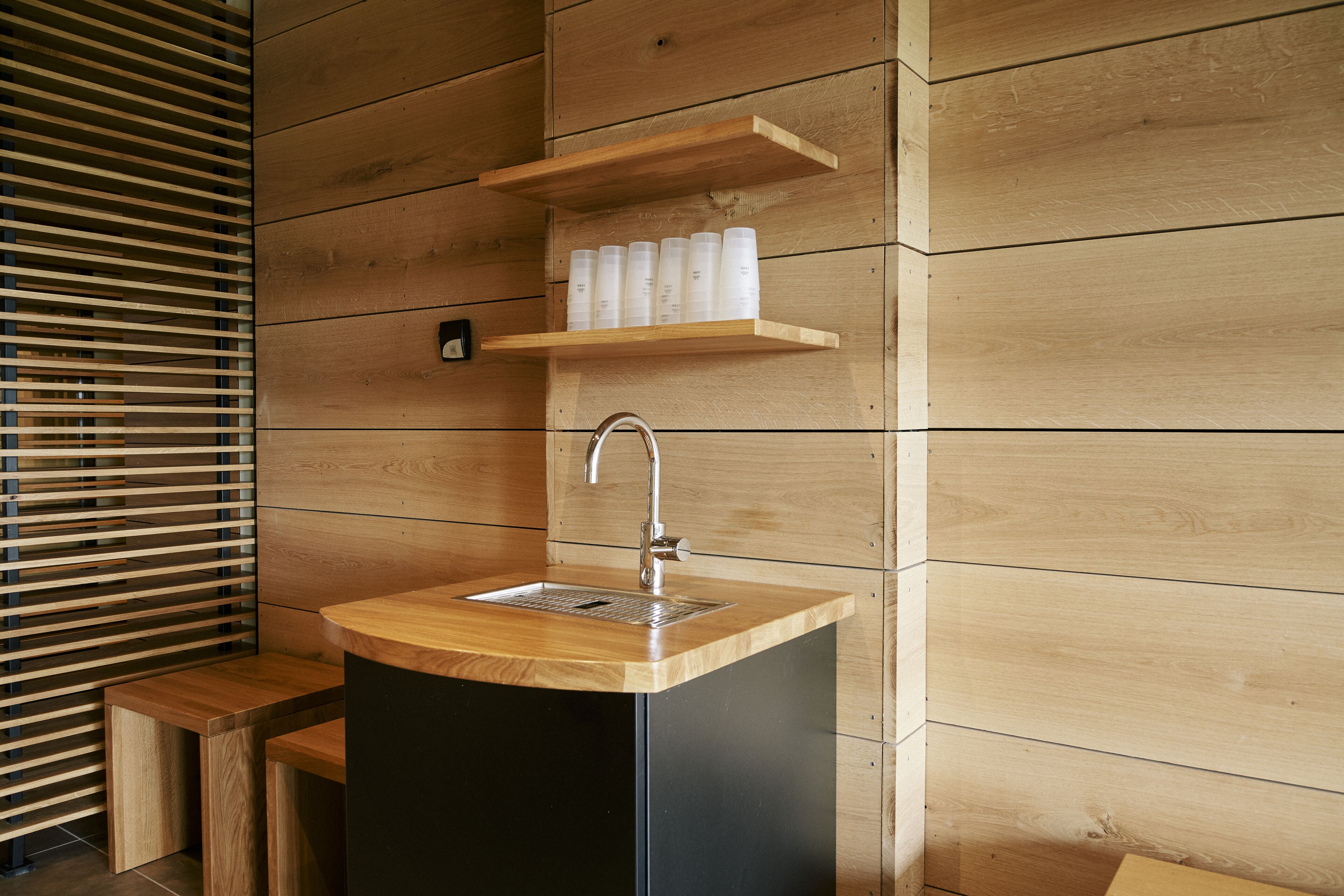 Ein Badezimmer aus Holz mit Waschbecken, Regalen und einer Bank.