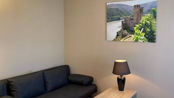 A modern room with a dark blue sofa, a wooden side table with a lamp, and a framed picture of a castle on the wall.