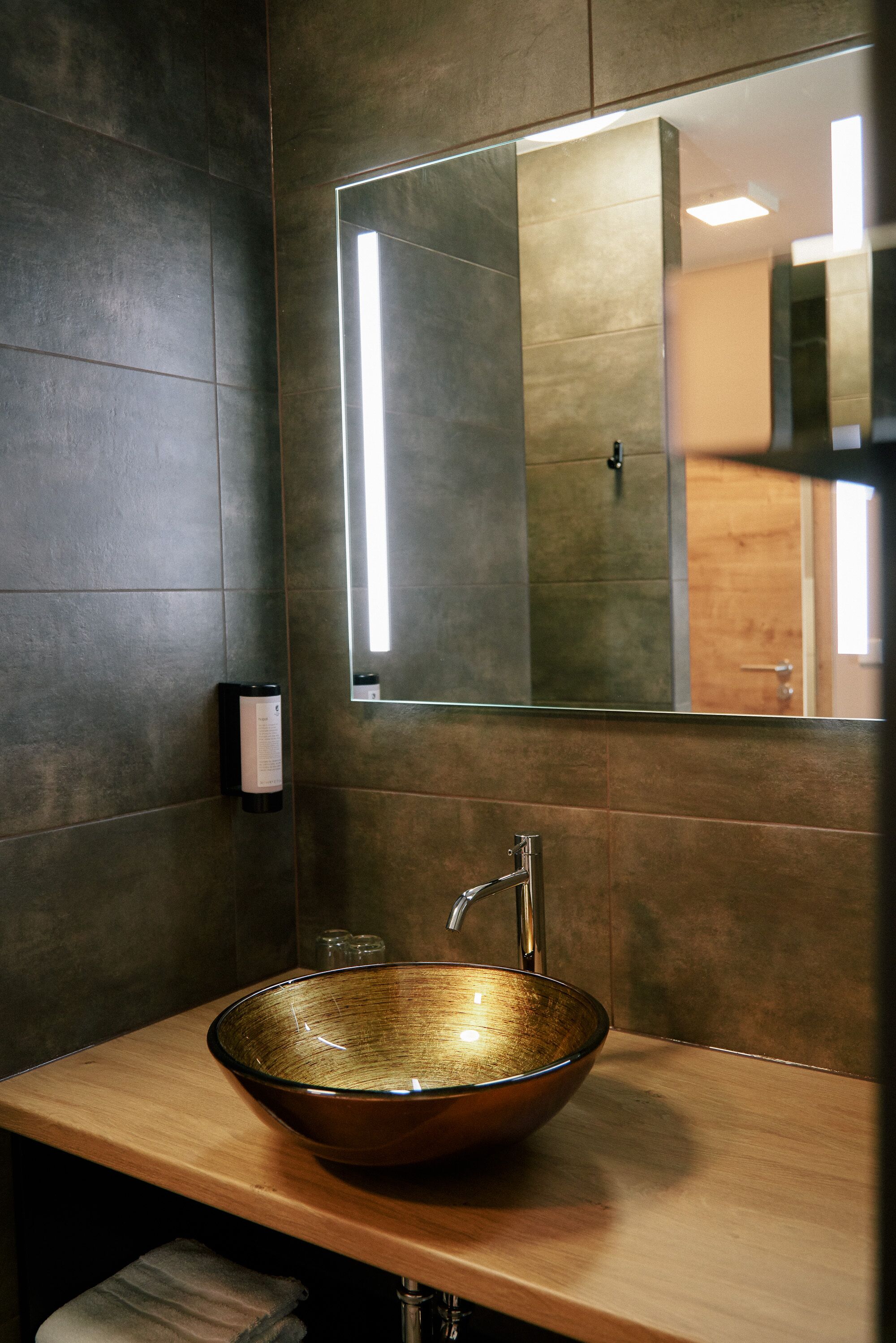 Un baño moderno con un espejo grande, un lavabo de cobre y una encimera de madera.