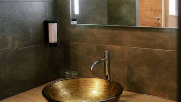 Un baño moderno con un espejo grande, un lavabo de cobre y una encimera de madera.