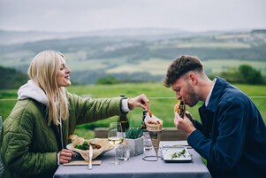 Deux personnes dînent en plein air, avec un paysage magnifique en arrière-plan.