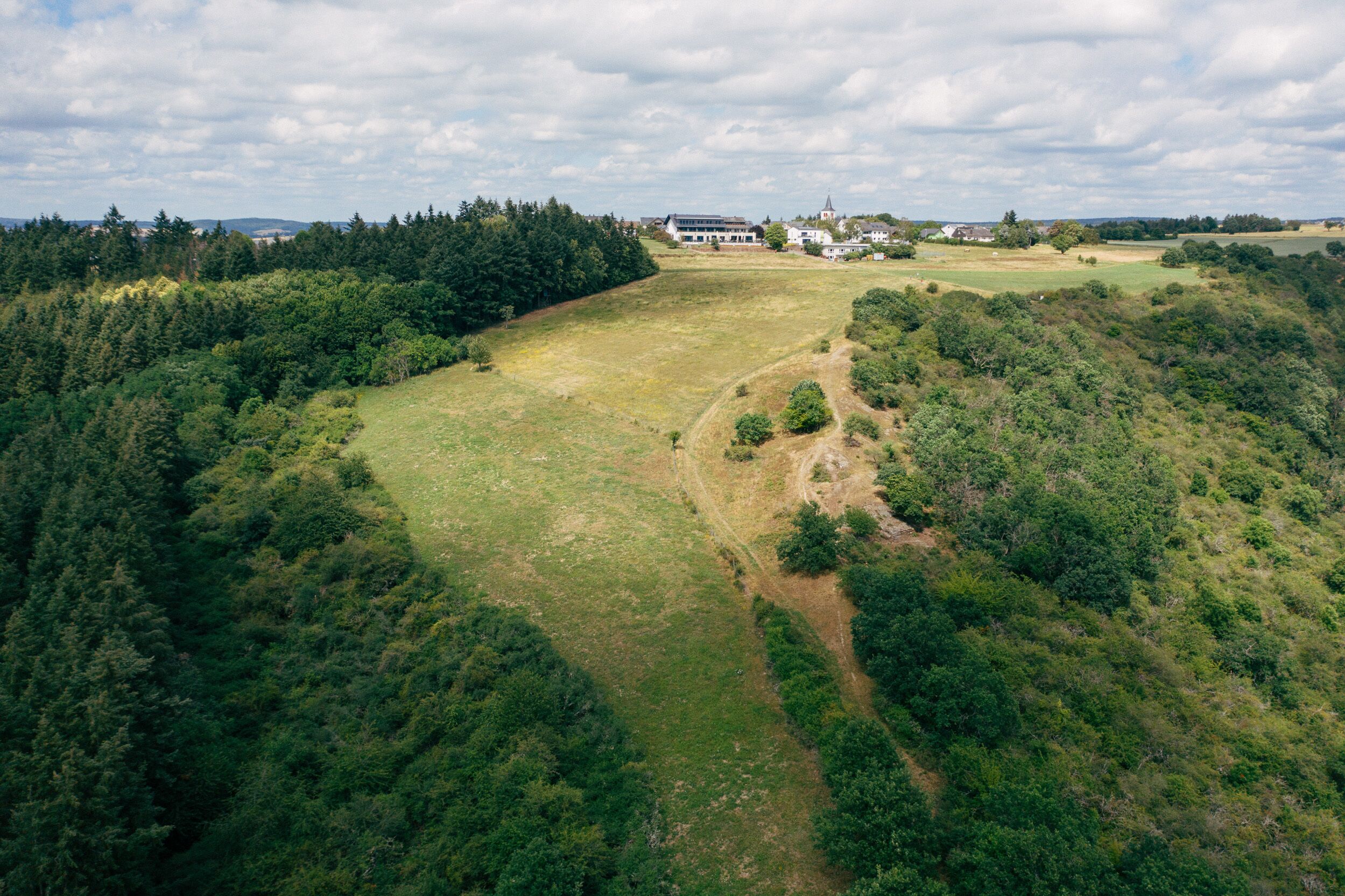 Ilmakuva maaseutumaisemasta, jossa on laaja avoin pelto, tiheä metsä ja muutamia rakennuksia kauempana.
