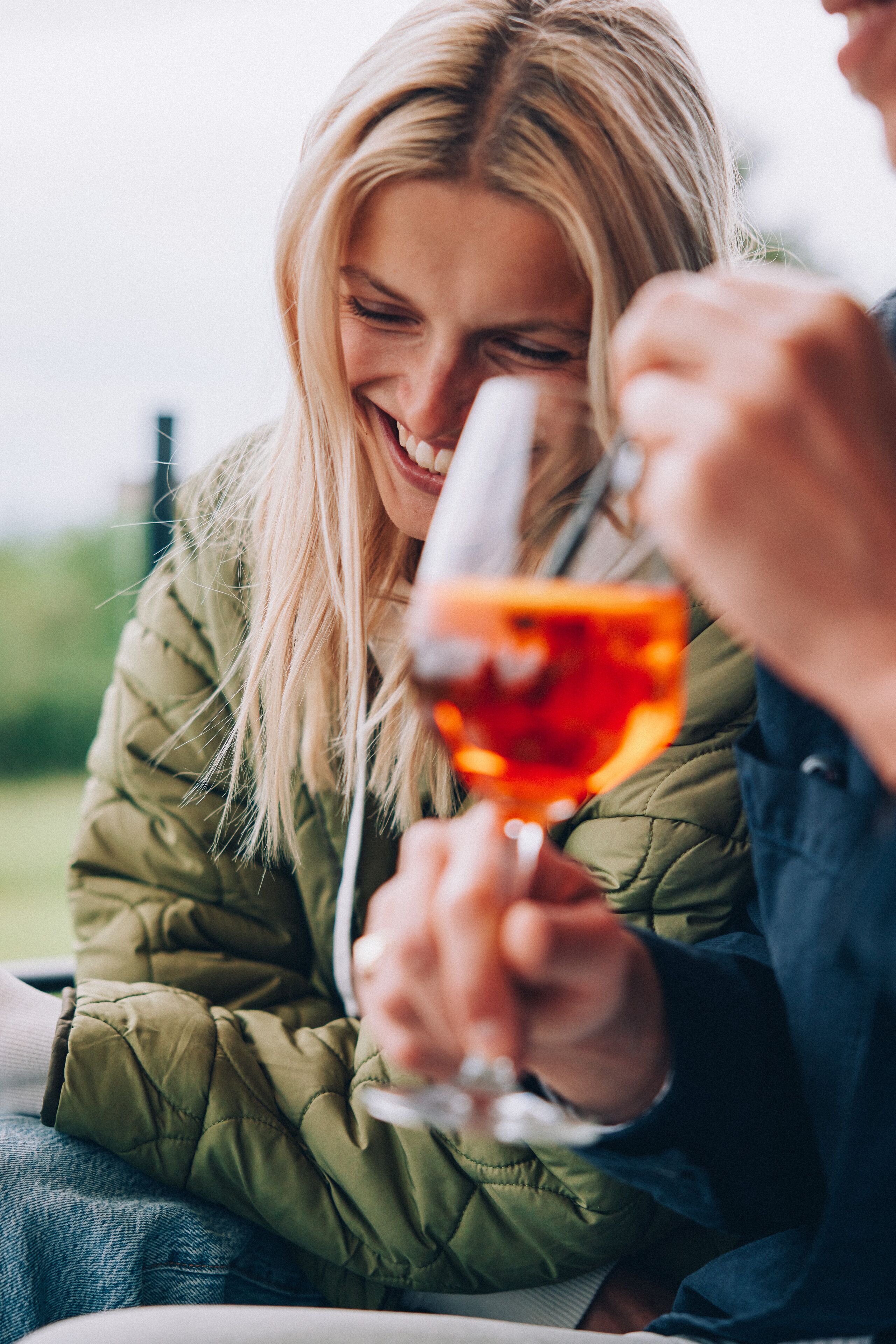 Une personne tenant un verre contenant un liquide rouge et portant une veste verte.