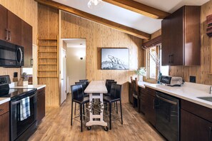 A modern kitchen with wooden walls, a dining table with chairs, and built-in appliances.
