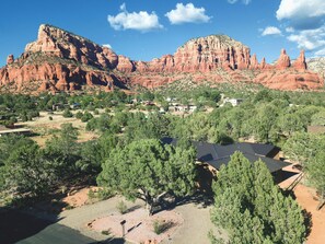 A residential area with houses surrounded by trees and red rock formations in the background.