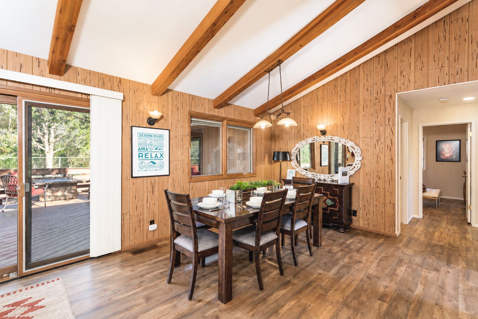 A dining area with a wooden table and chairs, a mirror, and a framed sign on the wall.