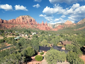 A rural landscape with red rock formations, scattered houses, and dense green trees.