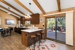 Eine moderne Küche mit Holzbalken, einer Bar mit Hockern und einer Glastür, die auf eine Terrassenausläufer führt.