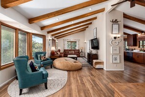 A spacious living area with wooden beams, a large sofa, a teal armchair, and a round ottoman.