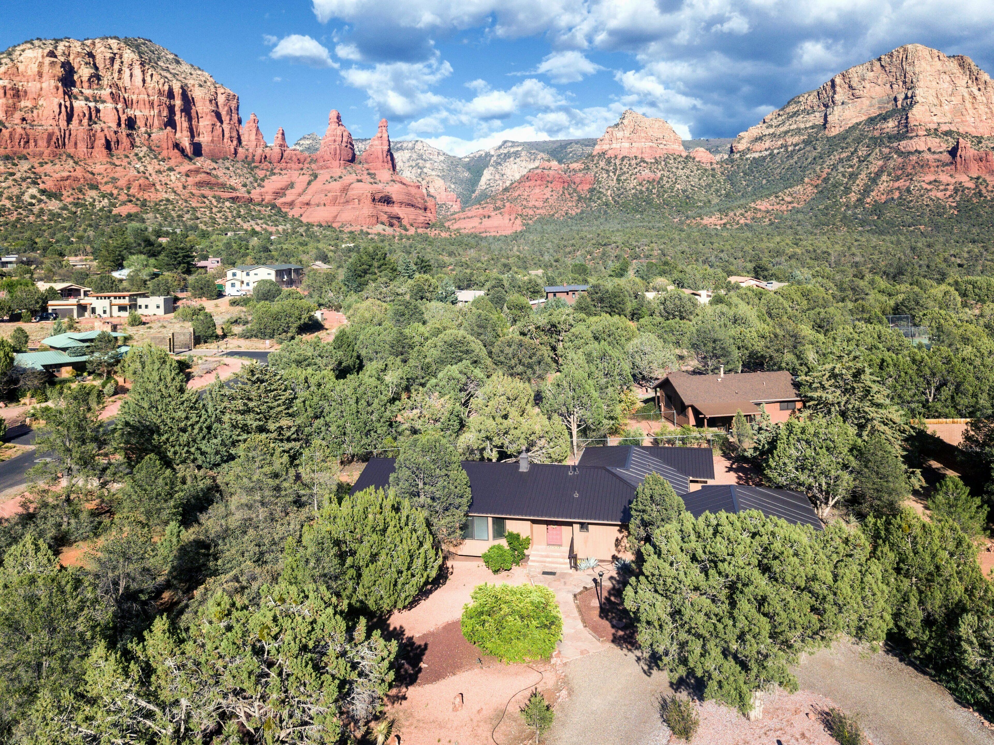 A residential area with houses surrounded by dense greenery and red rock formations in the background.