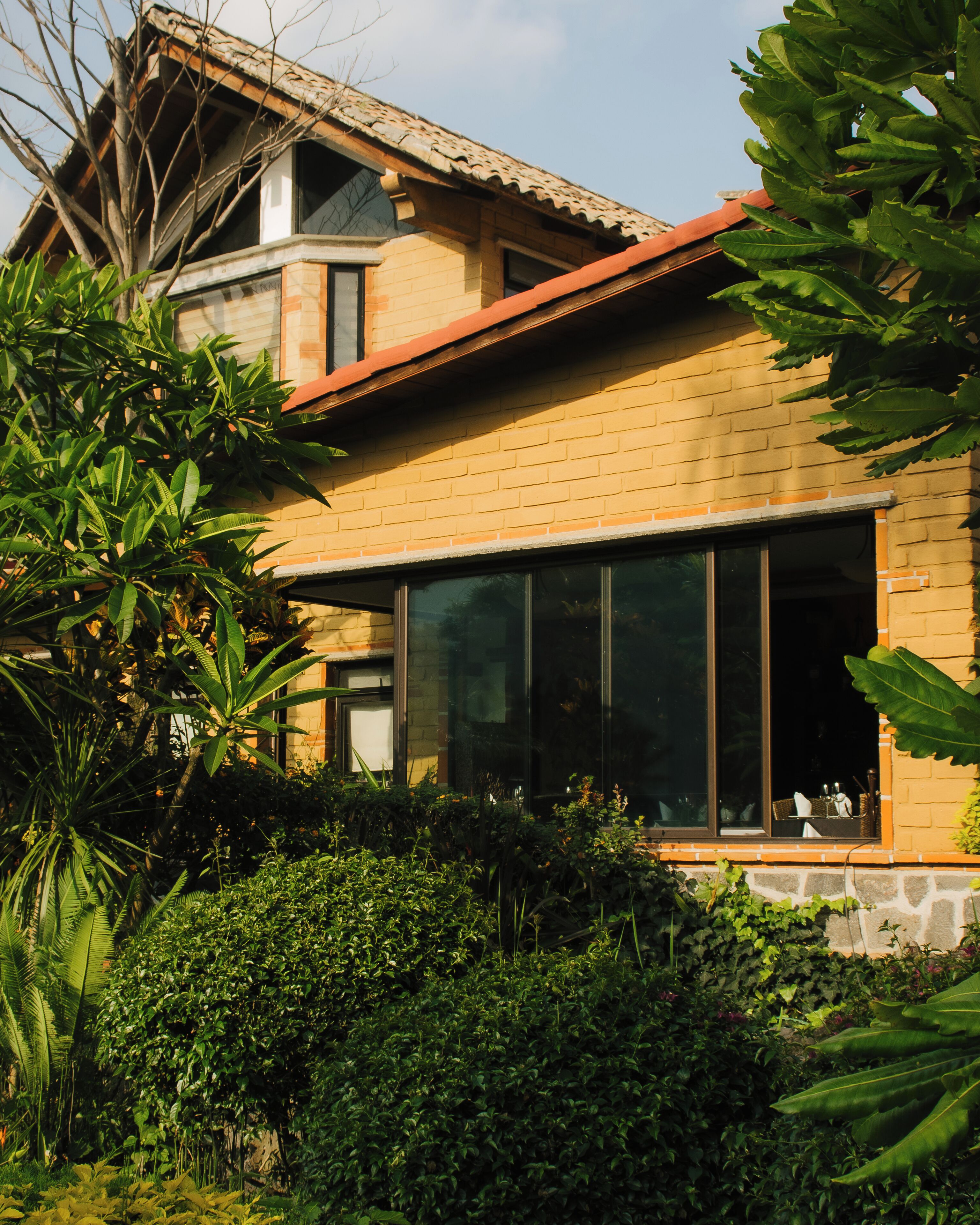 Una casa de dos plantas con fachada de ladrillo, ventanas grandes y techo rojo.