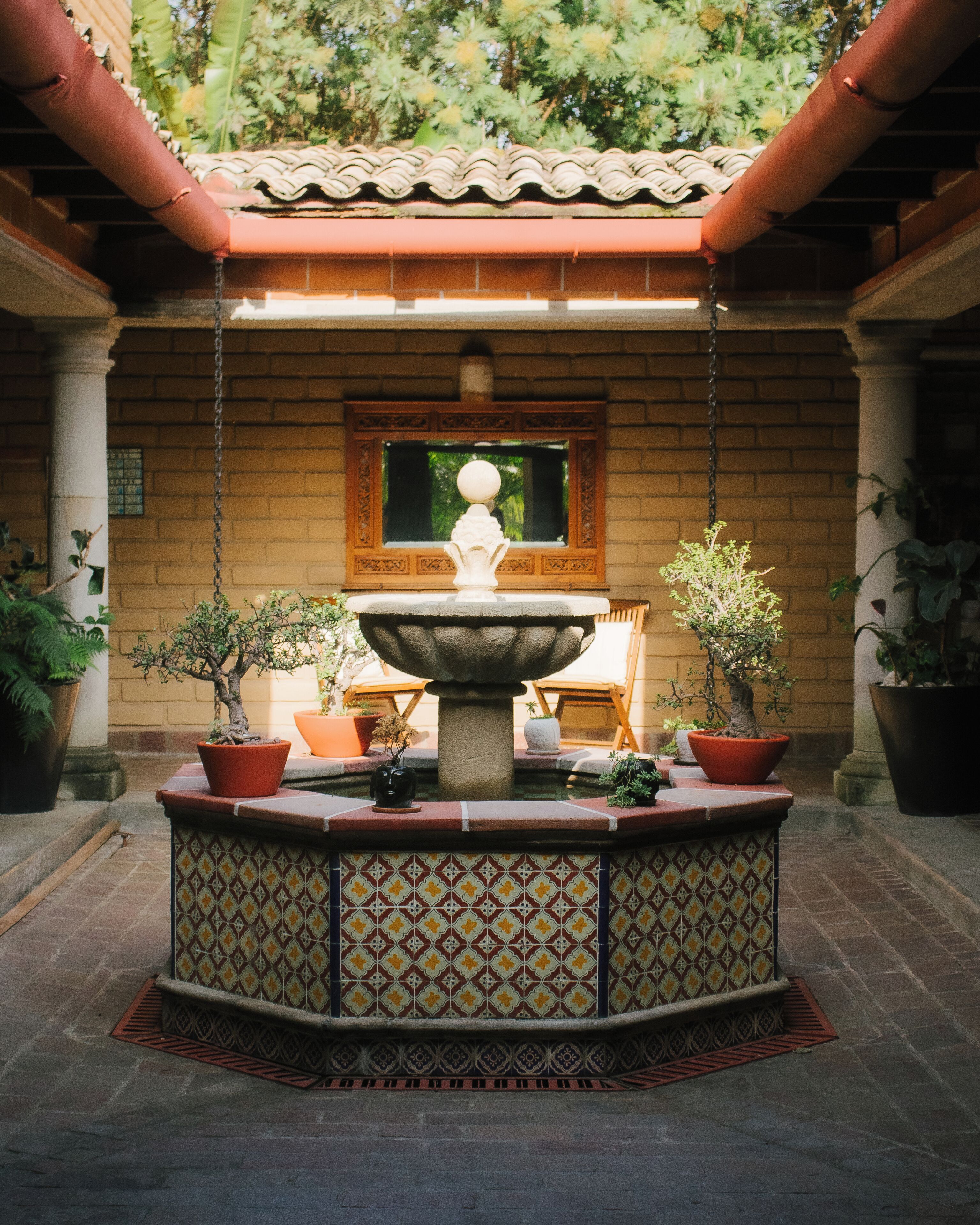 A courtyard with a central fountain, surrounded by potted plants and a tiled floor.