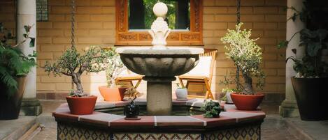 A courtyard with a central fountain, surrounded by potted plants and a tiled floor.