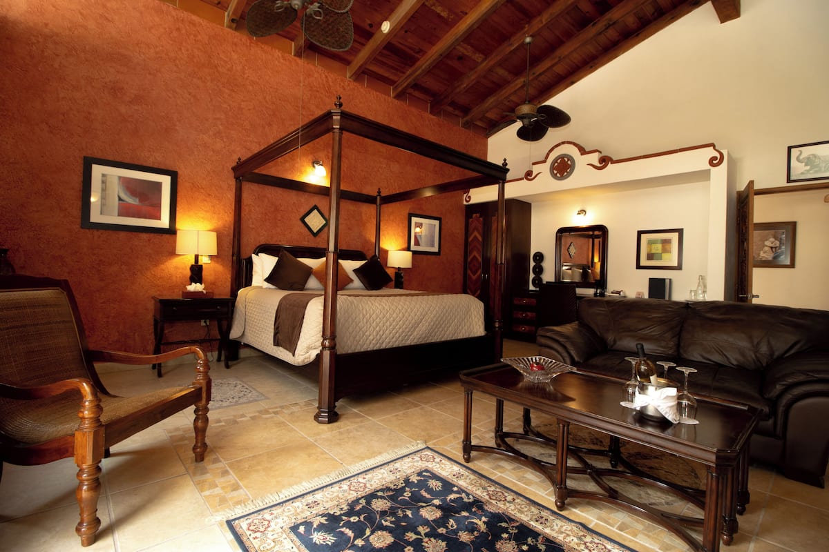 A traditional four-poster bed with a wooden frame and a matching headboard, a leather sofa, a wooden coffee table, and a patterned rug.