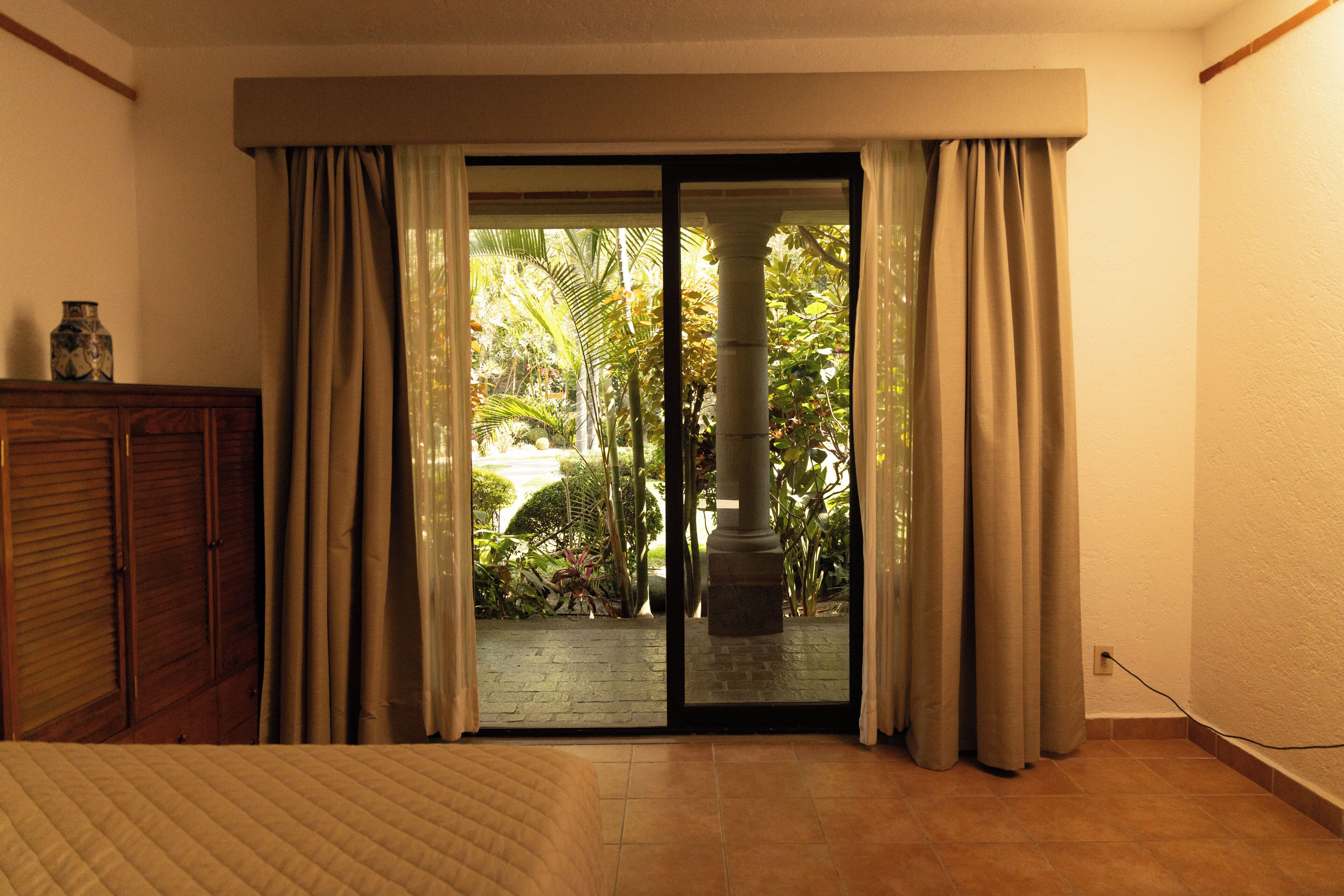 A room with a bed, a wooden cabinet, and a sliding glass door leading to a garden.