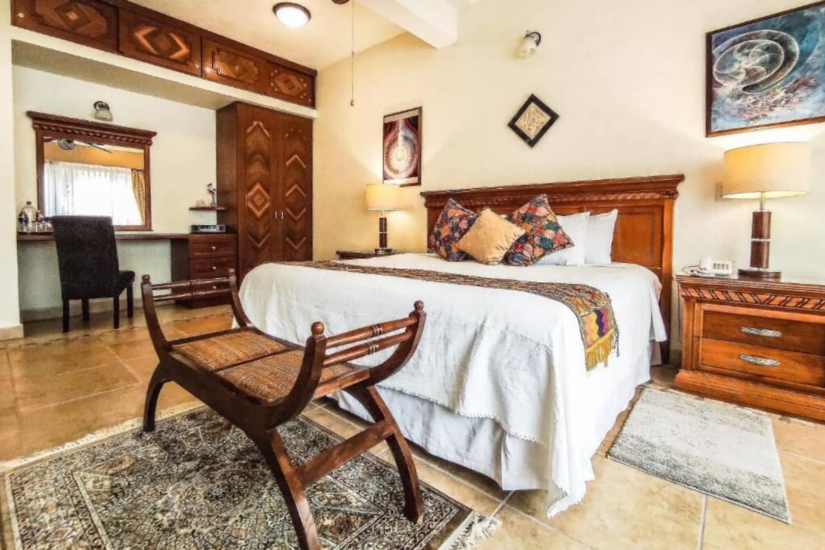 A bedroom with a large bed, wooden furniture, a desk, and a chair.