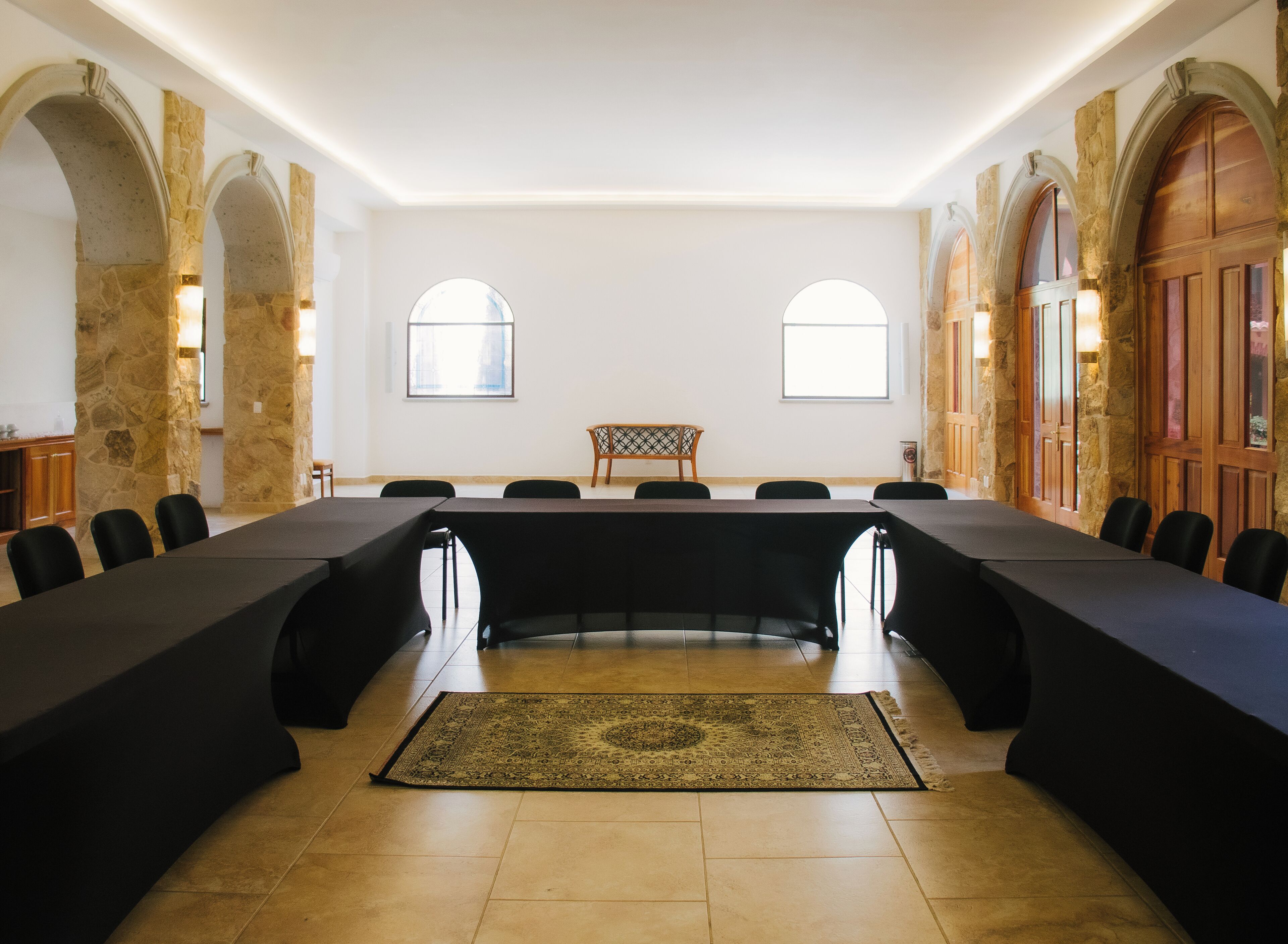 Un salón de conferencias con una larga mesa, sillas negras, paredes de piedra y arcos.