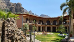 A courtyard with a pool, palm trees, and a building with a tiled roof and columns. - La Buena Vibra Wellness Resort & SPA (Tepoztlán)