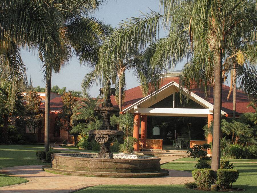A building with a covered patio, palm trees, and a fountain.