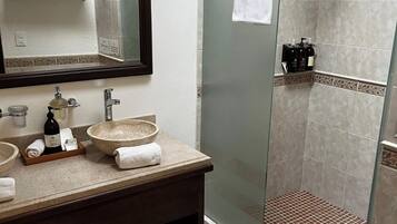 A modern bathroom with a glass-enclosed shower, a large mirror, and a vanity with a bowl sink.