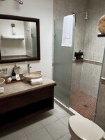 A modern bathroom with a glass-enclosed shower, a large mirror, and a vanity with a bowl sink.