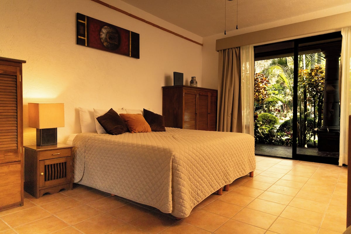 A bedroom with a bed, nightstand, and a view of a garden through a sliding glass door.