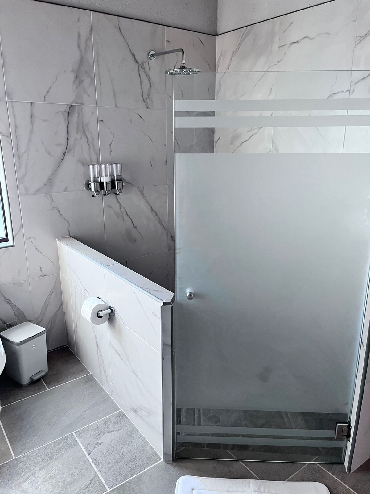 Un baño moderno con ducha envuelta en vidrio, pared de mármol blanco y retrete.
