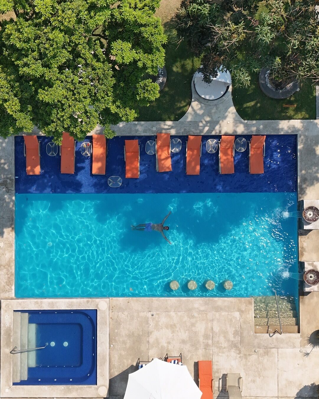 An aerial view of a rectangular swimming pool with lounge chairs and a hot tub.