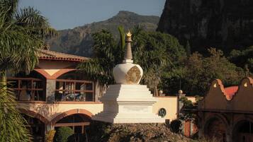 Un edificio tradicional con una estupa blanca, rodeado de palmeras y una colina rocosa.