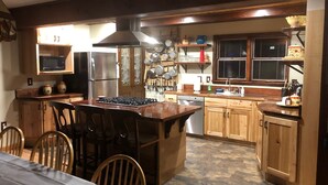Eine Küche mit Holzausstattung, einem Gasherd, einem Kühlschrank und einem Essbereich mit Stühlen und einem Tisch.