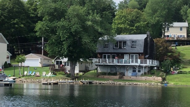 Ein zweistöckiges Haus mit Balkon, einem Steg mit Booten und einem See.